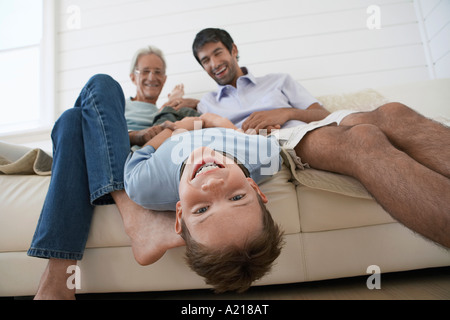 Boy hanging upside down off couch, with father and grandfather sitting beside him Stock Photo