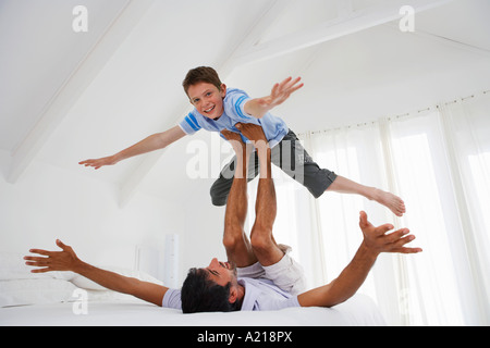 Son balancing on father's legs on bed in bedroom Stock Photo