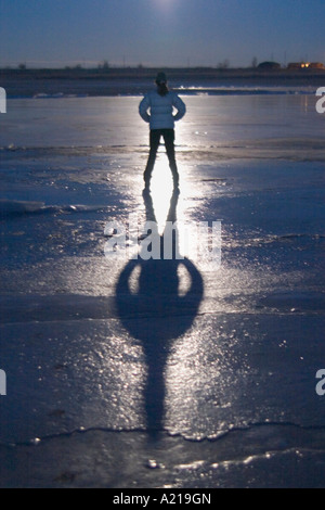 A woman standing on a frozen lake at night with her moon shadow in winter near Huntington Utah Stock Photo