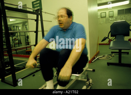 BALDING OVERWEIGHT MAN WITH GLASSES ON A ROWING MACHINE LONDON TAXI DRIVERS ASSOCIATION GYM Stock Photo