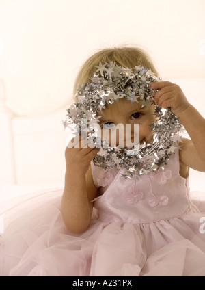 Toddler wearing a pink party dress peeking through a tinsel halo Stock Photo