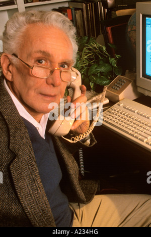 Elderly man sitting at the computer and talking on the telephone Stock Photo