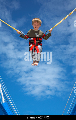 young child bouncing on bungee trampoline gymnastic apparatus against blue sky in the summer Stock Photo