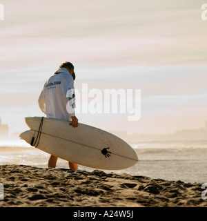 A surfer carries his board under dramatic morning skies on a the beach at Playa Bruja Mazatlan Mexico Stock Photo