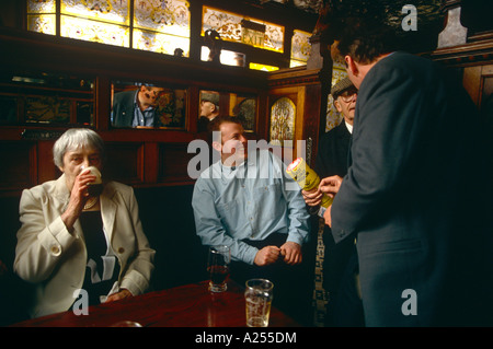 Drinkers in Belfast's Crown Bar in Great Victoria Street enjoy a pint of beer and talk with a charity worker. Stock Photo