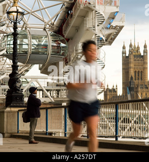 A jogger runs past The London Eye Millennium Wheel on  London's South Bank in the evening 2006 Stock Photo