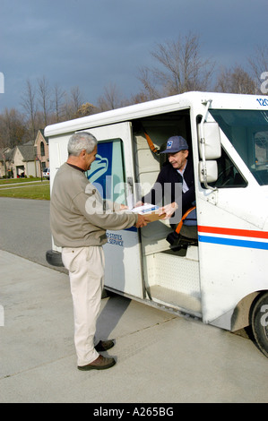 Postal carrier driving a mail truck delivers mail to male home owner Stock Photo