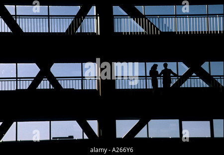 2 backlit people discuss the day's events on a walkway in a large corporate skyscraper. Stock Photo