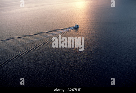 A tiny  craft makes its way through the calm glass water as the morning sun rises creating a beautiful reflection on the surface Stock Photo