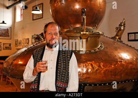 A man enjoys a glas of whiskey behind an old pot still (a giant copper kettle) used for the distillation in the Bushmills Stock Photo