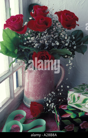 Red roses in pink pitcher in window Stock Photo