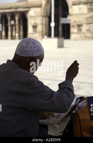 A Muslim man wearing traditional skull cap is sewing in front of Jama or Jami Masjid; the picture is a near-silhouette Stock Photo