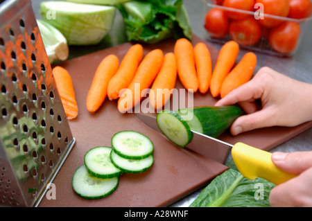A CHEF SLICES A CUCUMBER ON A CHOPPING BOARD READY TO PREPARE A SALAD FOR NEW HEALTHY SCHOOL DINNERS UK Stock Photo