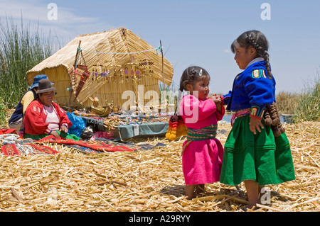 2 young girls dressed in traditional clothes with mum in the background on one of the reed islands on Lake Titicaca. Stock Photo