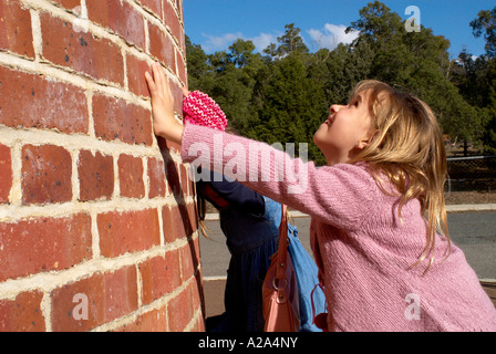 8 year old female child leaning against brick chimney stack, younger child in background Stock Photo