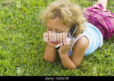 Child using mobile phone lying on lawn Stock Photo