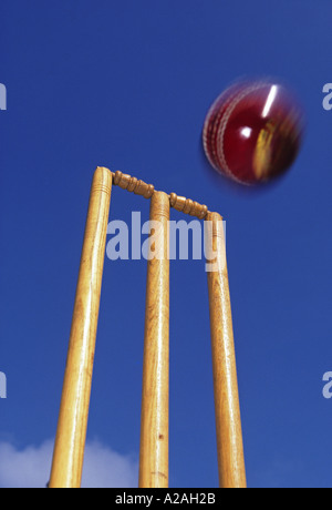 Close up of red cricket ball about to strike the stumps set against a blue sky Stock Photo