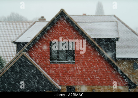 Roof shapes & gable ends close up twice on house with window & smaller gable over garage during a snow storm late winter early spring Essex England UK Stock Photo