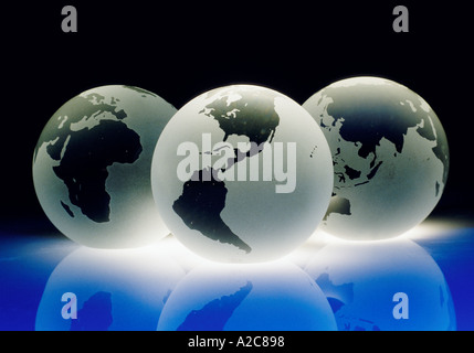 Three crystal earth globes representing the different parts of the world reflecting a blue light from underneath Stock Photo