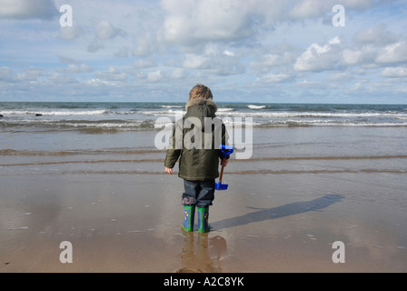 A young boy watches the tide coming in on Croyde beach North Devon England