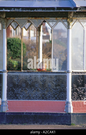 Small boy looking out through broken pane of Victorian Shelter on the promenade in Lytham St Annes Stock Photo