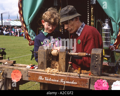 Man turning wood on old lathe with young lad helping Stock Photo