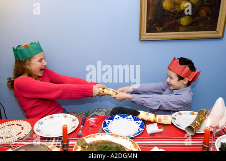 Brother and sister pulling Christmas cracker at the lunch table England UK Stock Photo