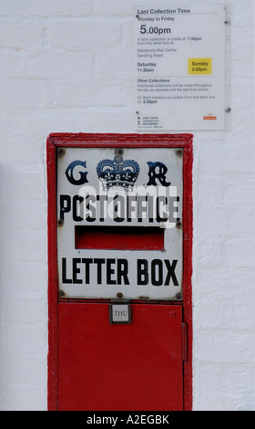 Red letter box set in a white painted brick wall with a black and white enamel sign saying GR Post Office Letter Box Stock Photo