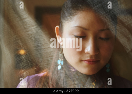 Close-up of a young woman with her eyes closed hiding behind a transparent curtain Stock Photo