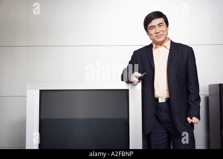 Portrait of a businessman standing by the side of a television smiling Stock Photo