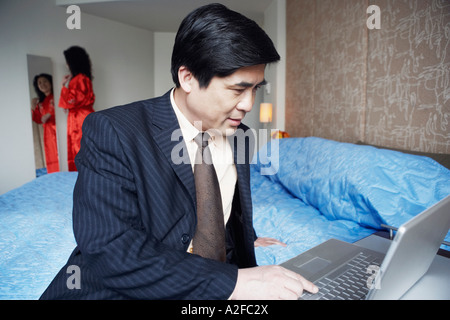 Close-up of a businessman sitting on the bed and using a laptop Stock Photo