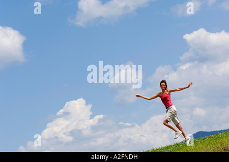 Young woman jumping in meadow, arms outstretched Stock Photo