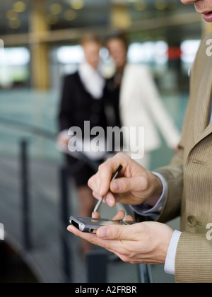 Young businessman using mobile phone, women talking in background Stock Photo