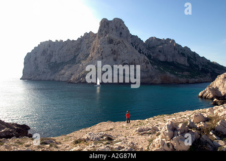 349 a little boy stands on a cliff overlooking a bay and island, watching a passing sailing boat Stock Photo