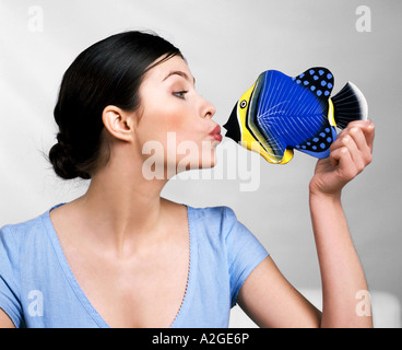 1216561 indoor studio young woman 20 25 brunette hair brown t shirt blue profile kiss mime face funny hand fish yellow h Stock Photo