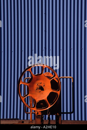 Close up of an orange fire hose reel in front of the corrugated steel exterior of a building Stock Photo