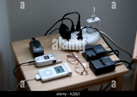 Electrical cords lead to multiple outlet extension cord to charge batteries for cameras cell phones and an Apple iPod. Stock Photo