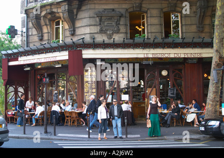 Le Bistrot du Peintre cafe bar terrasse terasse outside seating on the sidewalk. People sitting in chairs at tables eating and drinking outside at lunch time. People standing in front of a pedestrian crossing waiting for traffic The Bistrot du Peintre is an old fashioned Paris café cafe bar restaurant of art nouveau design with polished brass, mirrors and old signs Stock Photo