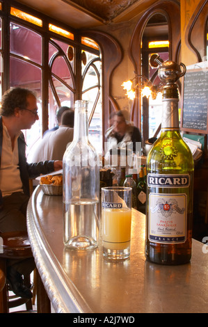 A bottle of Ricard 45 pastis and a glass and a carafe of water on a zinc bar in a cafe bar in Paris. In the background people si Stock Photo