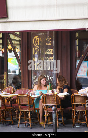 Le Bistrot du Peintre cafe bar terrase outside seating on the sidewalk. Two young women having a drink and chatting on a wicker Stock Photo