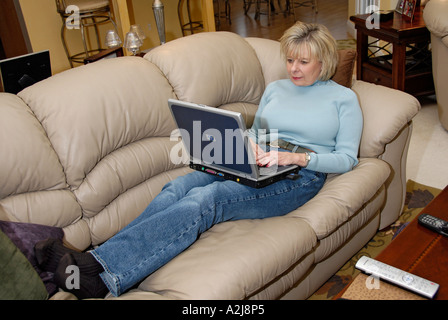 Female relaxes using a laptop computer and a wireless connection to the internet while in her home Stock Photo