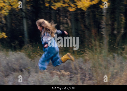 A young girl runs through a field by a woods Stock Photo