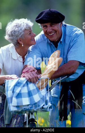 Mature couple leaning against a bicycle with a basket of baguettes Stock Photo