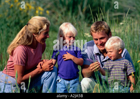 A mother and father introduce their son and daughter to purple flowers in a sunny field Stock Photo