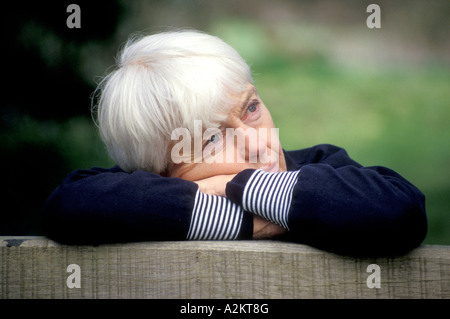 sad looking mature white haired woman leaning over edge of gate Stock Photo