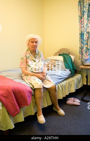 unhappy elderly lady in nursing home sitting on edge of bed