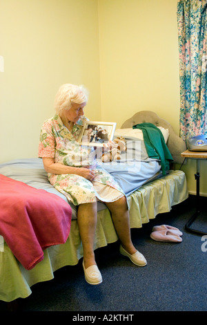 geriatric/old lady sitting on edge of bed in nursing home looking at family photo
