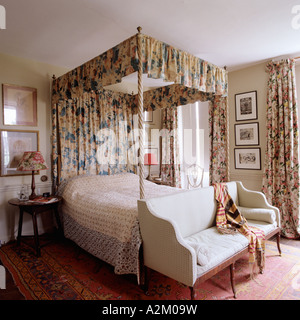 Bedroom with fourposter bed with floral curtains and settee with bolster Stock Photo