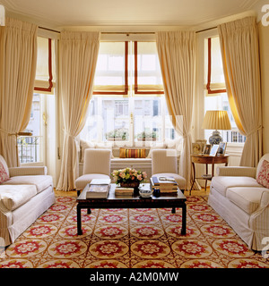 Large living room with three sofas, patterned carpet and bay windows Stock Photo