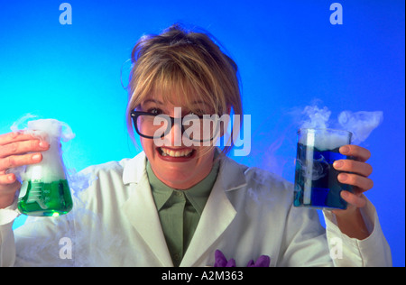 Portrait of a mad female scientist holding beakers with colored fluids wearing black rimmed glasses and a white lab coat Stock Photo